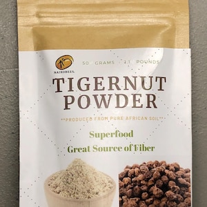 May include: A tan pouch of Tigernut Powder, a superfood, with the text "NAIROBEES" and "50 GRAMS : 1.1 POUNDS". The pouch features images of the powder in a wooden bowl and tigernuts. The text also reads "Great Source of Fiber".