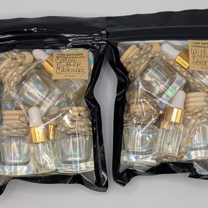 K&ouml;nnte beinhalten: Zwei schwarze Plastikt&uuml;ten gef&uuml;llt mit Lufterfrischern f&uuml;r Autos. Jede T&uuml;te enth&auml;lt mehrere kleine Glasflaschen mit goldfarbenen Deckeln und Holzperlen. Eine T&uuml;te ist mit "Cocoa Butter Cashmere" beschriftet, die andere mit "Wild Honey Lavender".