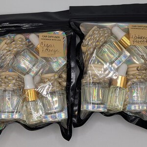 K&ouml;nnte beinhalten: Zwei schwarze Plastikt&uuml;ten mit Auto-Lufterfrischern. Jede T&uuml;te hat eine klare Glasflasche mit goldenem Verschluss und Pipette, zusammen mit einem Holzdiffusor und einem Etikett mit den D&uuml;ften "Cigar Lounge" und "Watermelon Punch".