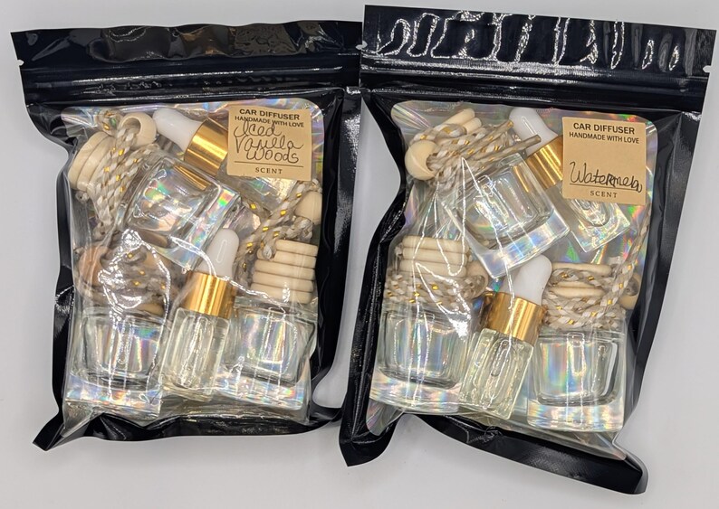 K&ouml;nnte beinhalten: Zwei schwarze Plastikt&uuml;ten gef&uuml;llt mit Auto-Lufterfrischern. Jede T&uuml;te enth&auml;lt kleine Glasflaschen mit goldfarbenen Deckeln, Holzperlen und einer Pipette. Eine T&uuml;te tr&auml;gt die Aufschrift "Iced Vanilla Woods", die andere "Watermelon".