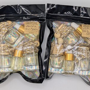 K&ouml;nnte beinhalten: Zwei schwarze Plastikt&uuml;ten mit Auto-Lufterfrischern. Jede T&uuml;te enth&auml;lt kleine Glasflaschen mit goldfarbenen Deckeln, Holzperlen und eine dekorative Schnur. Eine T&uuml;te tr&auml;gt die Aufschrift "Jamaica Me Crazy", die andere "White Candy Cold Brew".