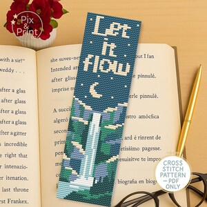 May include: A blue bookmark with the words "Let it flow" in white, featuring a waterfall design. The bookmark is on a book with a gold pen and glasses in the background. The bookmark is a cross stitch pattern.