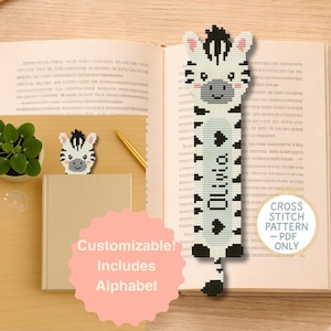 Op de afbeelding: Een handgemaakt kruissteek bladwijzer met zebra thema en een kleinere bijpassende zebra kop. De bladwijzer is wit met zwarte strepen en de naam "Olivia" erop gestikt. De afbeelding bevat ook een boek, een pen en tekst met de tekst "Aanpasbaar! Inclusief alfabet."