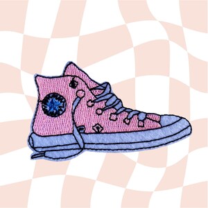 Puede incluir: Zapatillas rosas de caña alta con cordones azules y una estrella azul en el lateral. Las zapatillas están bordadas sobre un fondo a cuadros blanco y rosa.