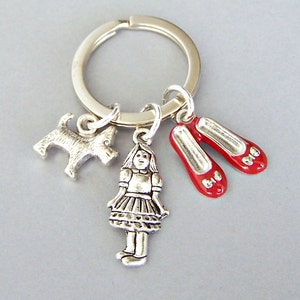 May include: Silver charm keychain with a silver dog, a silver girl in a dress, and two red ruby slippers.