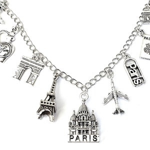 May include: Silver charm bracelet with various Parisian themed charms, including the Eiffel Tower, Arc de Triomphe, a perfume bottle, a passport, a plane, and a building that says "Paris".