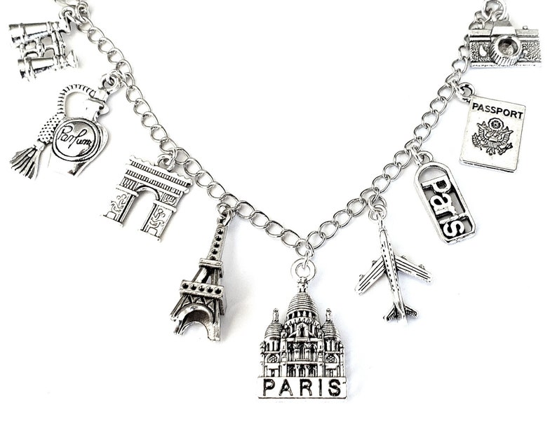 May include: Silver charm bracelet with various Parisian themed charms, including the Eiffel Tower, Arc de Triomphe, a perfume bottle, a passport, a plane, and a building that says "Paris".