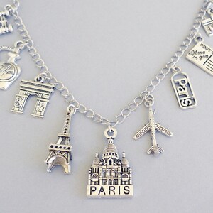 May include: Silver charm bracelet with Parisian themed charms, including the Eiffel Tower, the Arc de Triomphe, a perfume bottle, a camera, a postcard, a plane, and a church with "Paris" written on it.