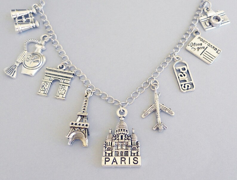 May include: Silver charm bracelet with Parisian themed charms, including the Eiffel Tower, the Arc de Triomphe, a perfume bottle, a camera, a postcard, a plane, and a church with "Paris" written on it.