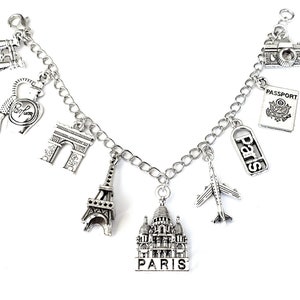 May include: Silver charm bracelet with Parisian themed charms, including the Eiffel Tower, Arc de Triomphe, a perfume bottle, a passport, a plane, and a building that says "Paris".