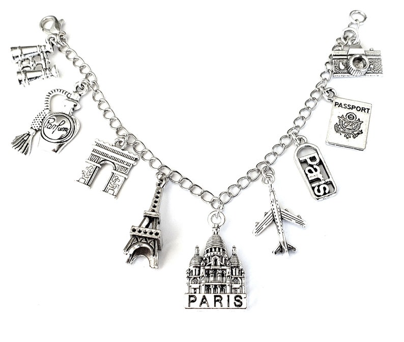 May include: Silver charm bracelet with Parisian themed charms, including the Eiffel Tower, Arc de Triomphe, a perfume bottle, a passport, a plane, and a building that says "Paris".
