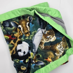 May include: A green and black fleece blanket with a satin trim. The blanket features a variety of animals including a giraffe, panda, tiger, and monkey.