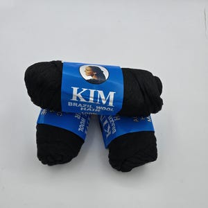Könnte beinhalten: Drei schwarze Rollen Kim Brazil Wool Hair, 100% Wolle, mit einem blauen Etikett, auf dem eine Frau mit einem Pferdeschwanz und der Markenname abgebildet sind.