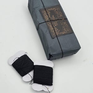 May include: Two spools of black thread wrapped in white paper with the text "Celluloid" on a brown paper package.