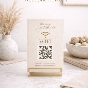 Puede incluir: Un letrero beige con texto dorado que dice "Welcome to Our Airbnb" y "WIFI". Incluye un código QR e información de la red. El letrero está en un soporte de metal dorado. La palabra "DOWNLOAD" está en la parte inferior.