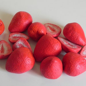 May include: A group of red strawberries, some whole and some cut in half, arranged on a white surface.