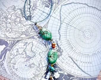 May include: A handcrafted necklace featuring large, oval-shaped turquoise stones, interspersed with smaller beads in shades of orange, blue, and gold. The necklace is displayed against a vintage map background, showcasing a unique, bohemian style.