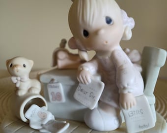 May include: A porcelain figurine of a child sitting at a desk with a small cat. The child holds a paper labeled Dear Sir and another labeled Bills with the word total. A calendar shows Friday 10, and papers are scattered on the floor.