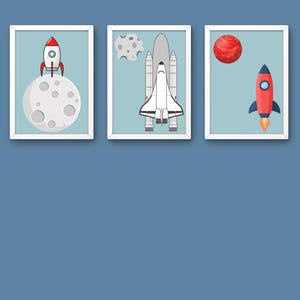 Puede incluir: Tres láminas enmarcadas con temática espacial. La primera muestra un cohete rojo y blanco en la luna. La segunda muestra un transbordador espacial y un asteroide gris. La tercera muestra un planeta rojo y un cohete rojo y azul.