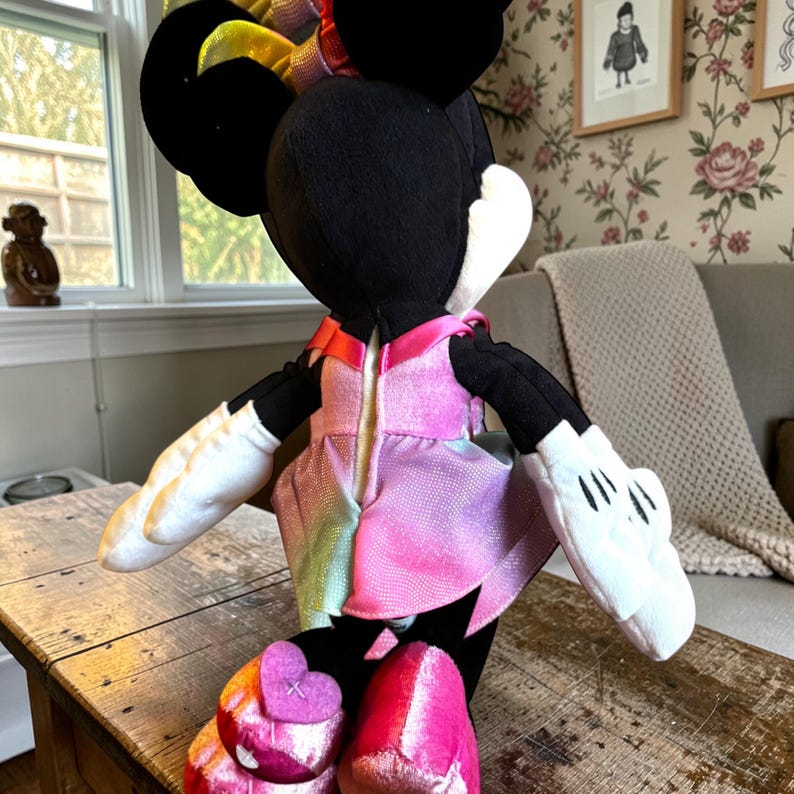 A plush toy of Minnie Mouse dressed in a pink dress is sitting on a wooden table.
