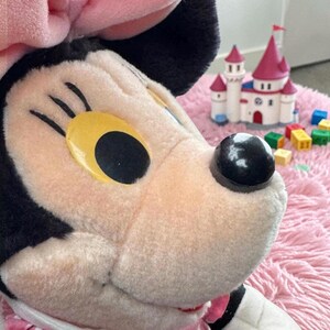A close-up of a stuffed Minnie Mouse toy with a pink and white castle in the background.