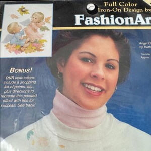 The image is a promotional poster for a product called "Full Color Iron-On Design by FashionArt". The poster features a smiling woman with a turtleneck sweater, and there is a small illustration of a baby angel on the left side of the poster.