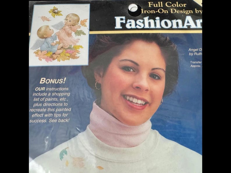 The image is a promotional poster for a product called "Full Color Iron-On Design by FashionArt". The poster features a smiling woman with a turtleneck sweater, and there is a small illustration of a baby angel on the left side of the poster.