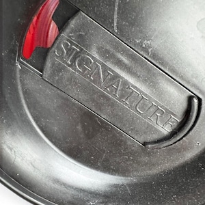 a close-up view of a black metal object with the word "SIGNATURE" engraved on it.