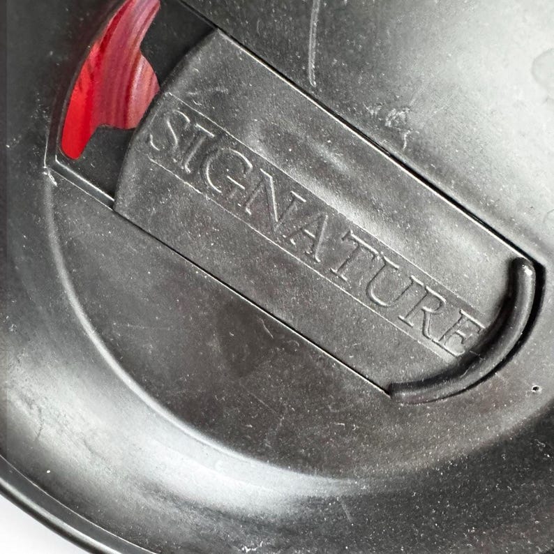 a close-up view of a black metal object with the word "SIGNATURE" engraved on it.