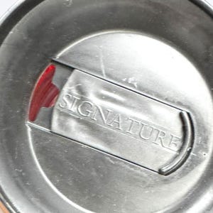 a close-up view of a metal container with the word "SIGNATURE" engraved on it.