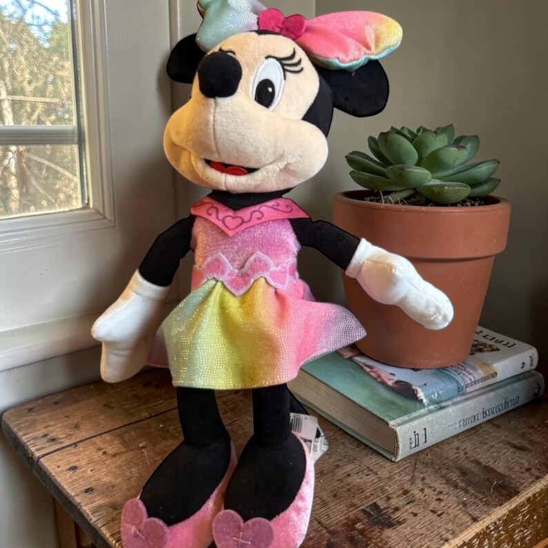 A Minnie Mouse plush toy is sitting on a wooden surface next to a potted succulent plant and some books.