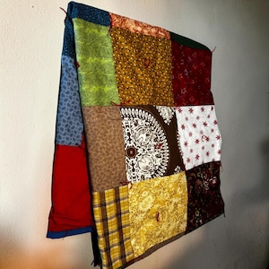 May include: A patchwork quilt featuring a variety of fabric squares in colors including mustard yellow, lime green, deep red, brown, and white. The squares display diverse patterns such as paisley, floral, plaid, and a central circular mandala design.