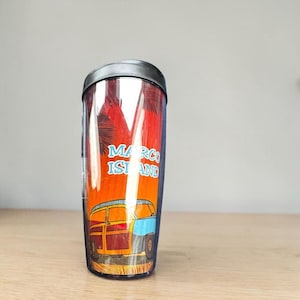 A tall, clear tumbler with a printed design of a car and palm trees on it, sitting on a wooden surface.