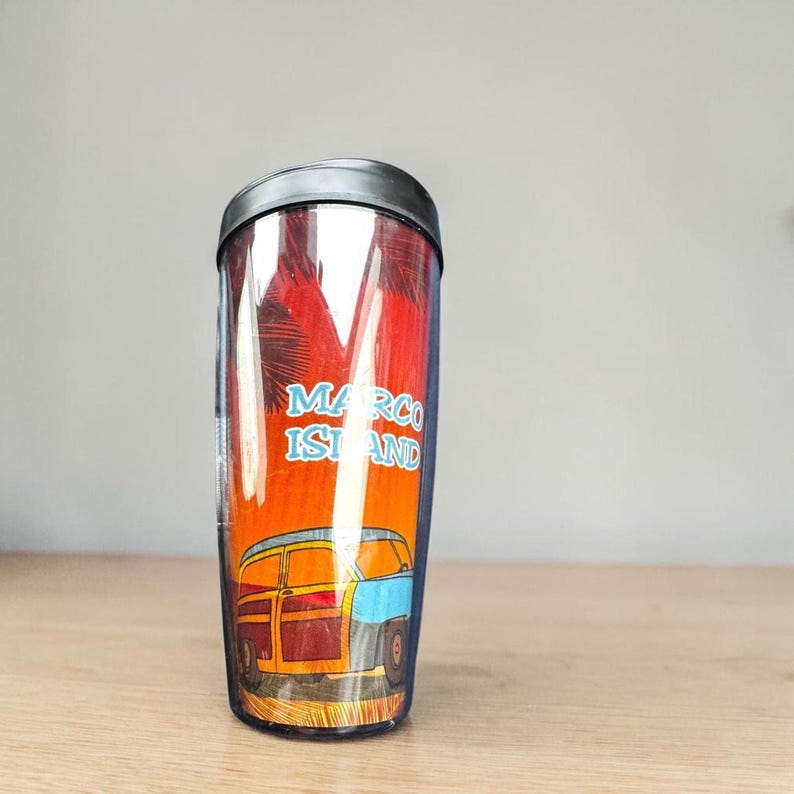 A tall, clear tumbler with a printed design of a car and palm trees on it, sitting on a wooden surface.