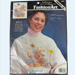 The image is a package for Iron-On Design by FashionArt, featuring a smiling woman with a white sweater adorned with a design of cherubs and leaves.