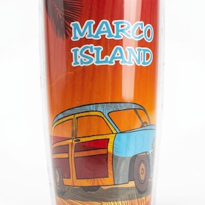 A colorful glass tumbler with a tropical island design, featuring a car illustration and palm trees.