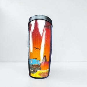 A tall, clear glass tumbler with a colorful, printed design depicting a car, palm trees, and a sunset on its surface.