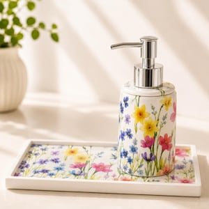 May include: A ceramic soap dispenser and tray set. The dispenser features a silver pump and is adorned with a vibrant floral pattern of yellow, pink, and blue flowers. The matching tray has a similar floral design.