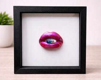 Puede incluir: Obra de arte enmarcada que presenta unos labios magenta brillantes con una pastilla azul y blanca en su interior. La pastilla tiene la palabra "Chill" impresa. La obra está sobre un fondo blanco dentro de un marco negro.