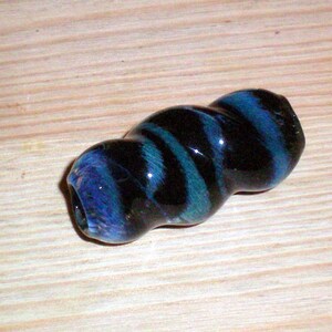May include: A black and blue glass bead with a swirled pattern. The bead is about 2 inches long and has a glossy finish.