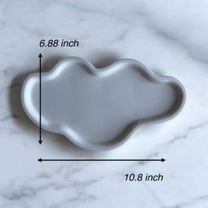 以下が含まれることがあります： 灰色の雲型のセラミックトレイ。トレイの長さは27.4cm、幅は17.5cmです。トレイは滑らかな表面で、丸みを帯びたエッジで設計されています。トレイは白い大理石の表面にあります。