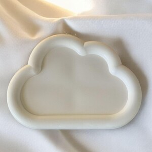 May include: A white cloud-shaped tray made of a solid material. The tray has a smooth, rounded edge and a shallow interior. The background is a white fabric with soft folds.