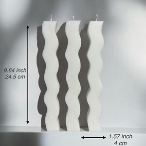 May include: Three white, wavy-shaped candles, each 9.64 inches (24.5 cm) tall and 1.57 inches (4 cm) wide. The candles have a unique, undulating design, and are arranged vertically against a neutral background. The wicks are visible at the top.