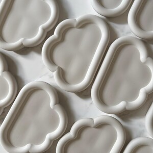 May include: A collection of white, cloud-shaped trays. Each tray has a rounded, oblong interior with a raised, scalloped edge. The trays are arranged on a light-colored, possibly marble, surface. The overall aesthetic is minimalist and modern.