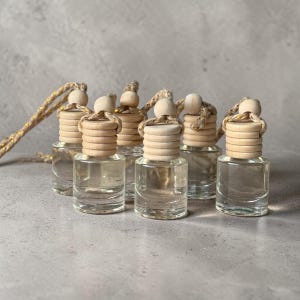May include: A collection of small, clear glass bottles with light-colored wooden caps and spherical wooden beads. Each bottle features a thick, ribbed wooden stopper and a hanging cord with subtle gold metallic threading woven throughout.