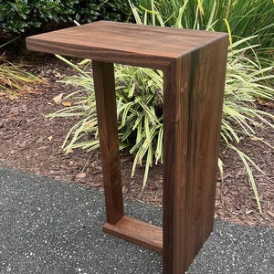 May include: A dark brown wooden side table with a rectangular top and a unique open frame design. The table is made of solid wood and has a natural finish.