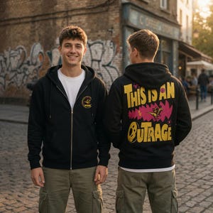 May include: A black zip-up hoodie featuring a small circular logo on the left chest and a large graphic on the back with the yellow text "THIS IS AN OUTRAGE" above a pink jagged shape and a small dinosaur illustration on a white t-shirt.