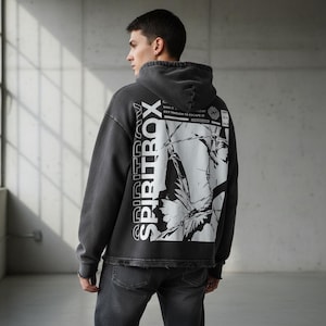 May include: A charcoal grey hoodie with the word "SPIRITBOX" printed vertically on the left side. The back features a large white graphic design with text and a butterfly motif. The hoodie has a drawstring hood and long sleeves.