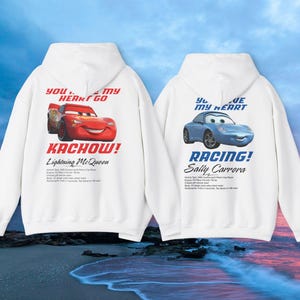 May include: Two white hoodies featuring cartoon car graphics. One displays a red car with "KACHOW!" and "Lightning McQueen" text. The other shows a blue car with "RACING!" and "Sally Carrera" text. Both have text that reads "YOU... MY HEART GO" and "YOU... MY HEART".
