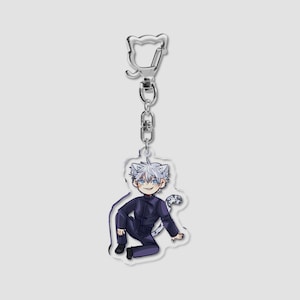 May include: A clear acrylic keychain featuring a cartoon character with white hair, blue eyes, and a black outfit. The keychain has a silver-colored clasp and chain, and the character is in a crouching pose with a cat tail.